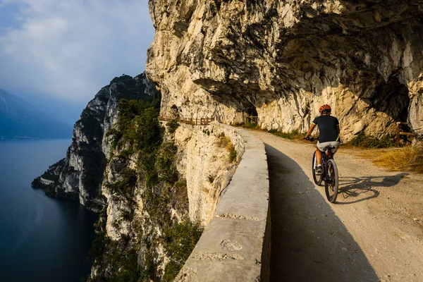 Cycling woman  riding on bikes at sunrise mountains and Garda lake landscape.  Cycling MTB enduro flow sentiero ponale trail track. Outdoor sport activity.