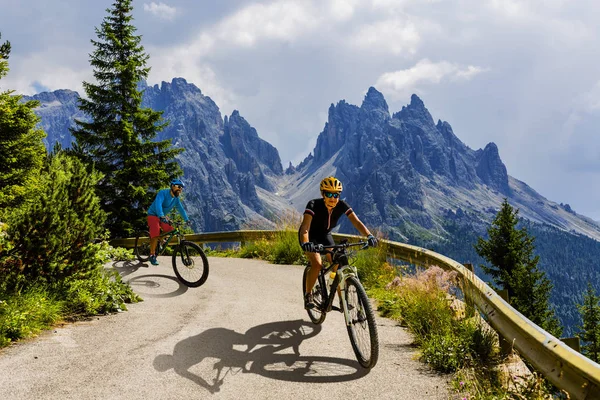 Cycling woman and man riding on bikes in Dolomites mountains and