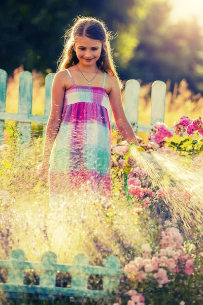 Ragazza giocosa che innaffia fiori con pioggia in giardino in estate — Foto Stock