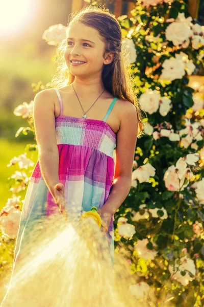 Playfull girl watering flowers with rain in the garden at summer — Stock Photo, Image