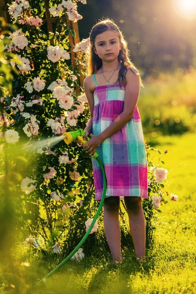 Играющая девочка поливает цветы дождем в саду летом — стоковое фото