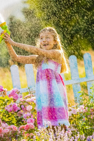 Lekfull tjej vattna blommor med regn i trädgården på sommaren — Stockfoto