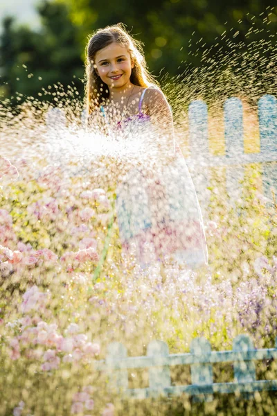 Lekfull tjej vattna blommor med regn i trädgården på sommaren — Stockfoto