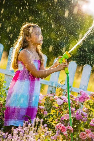 Playfull chica regando flores con lluvia en el jardín en verano —  Fotos de Stock