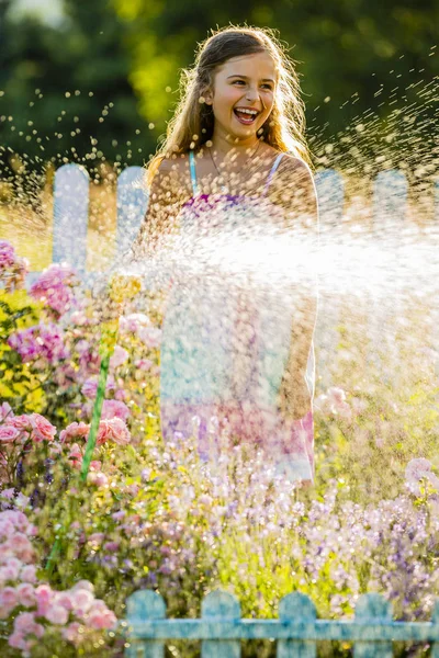 Hravá holka zalévání květiny s deštěm v zahradě v létě — Stock fotografie