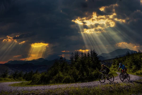 Fietsen van de vrouw en mannen rijden op de fiets bij zonsondergang bergen forest — Stockfoto