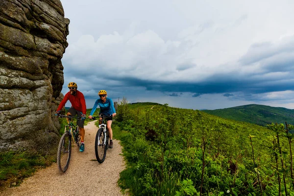 Cycling woman and men riding on bikes at sunset mountains forest landscape. Couple cycling MTB enduro flow trail track. Outdoor sport activity.