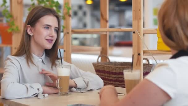 Dos mujeres jóvenes hablando y tomando café sentadas en la cafetería. — Vídeos de Stock