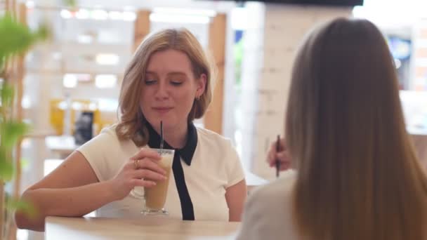 Dos mujeres jóvenes hablando y tomando café sentadas en la cafetería. — Vídeo de stock