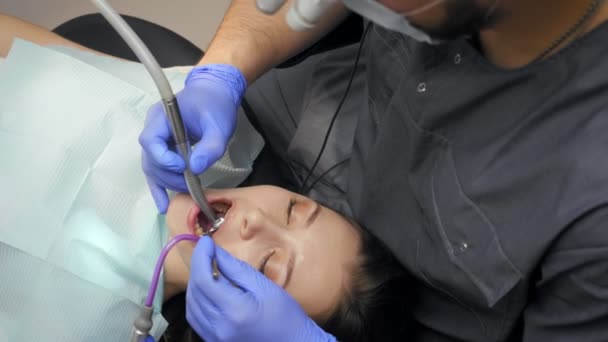 Male dentist treating teeth to young woman patient in clinic. — Stock Video