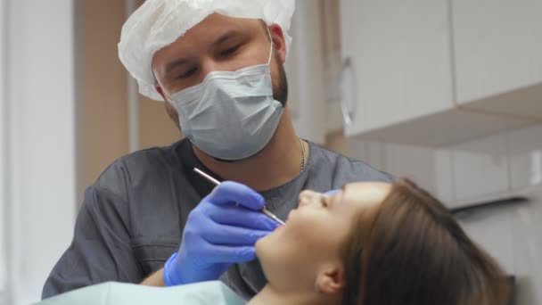 Male dentist treating teeth to young woman patient in clinic. — Stock Video