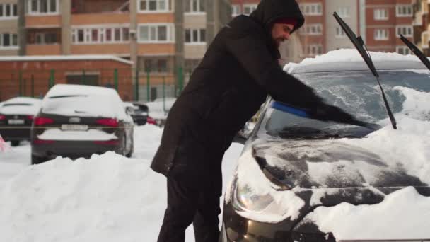 Man rensar sin bil med borste från snö på gården. — Stockvideo