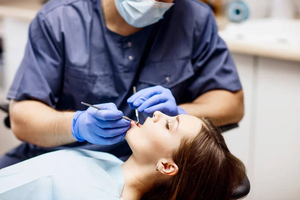 Odontólogo masculino tratando dientes a paciente joven en clínica . — Foto de Stock