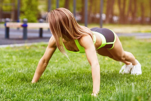 Mooie vrouw doen push-ups op het groene gras. — Stockfoto