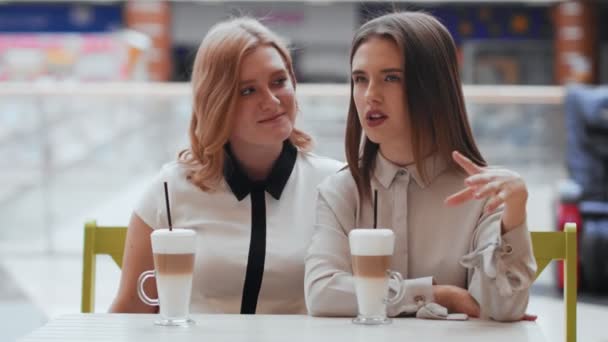 Két fiatal nő beszélget és kávézik a kávézóban.. — Stock videók