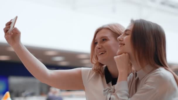 Två glada unga kvinnor att göra selfie i gallerian. — Stockvideo