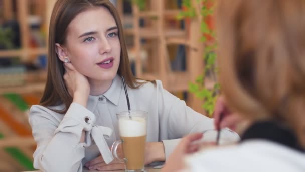 Две молодые женщины разговаривают и пьют кофе сидя в кафе. — стоковое видео