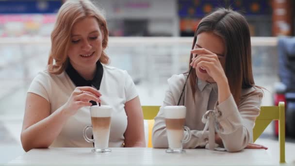 Dos mujeres jóvenes hablando y tomando café sentadas en la cafetería. — Vídeo de stock