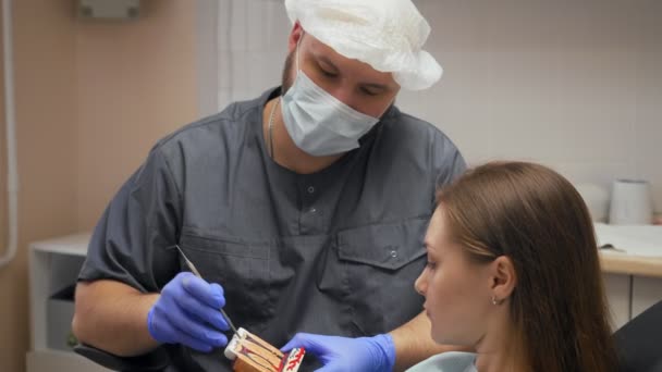 Мужчина дантист показывает и объясняет пациентке проблему на модели . — стоковое видео