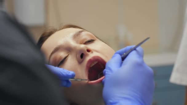 Male dentist treating teeth to young woman patient in clinic. — Stock Video