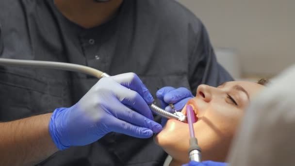 Male dentist treating teeth to young woman patient in clinic. — Stock Video