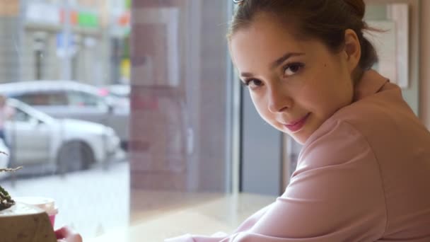 Młoda atrakcyjna kobieta uśmiechając się do kamery w kawiarni. — Wideo stockowe