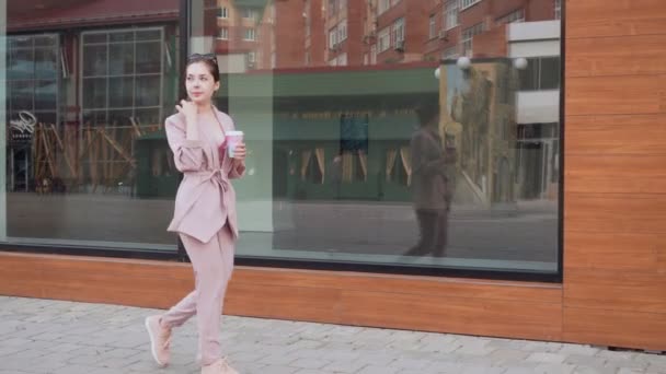 Stilvolle Frau, die auf der Straße läuft und eine Tasse Kaffee in der Hand hält. — Stockvideo