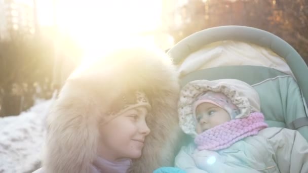 Schattig 1 jaar meisje in de kinderwagen wandelingen met oudere zus in de winter. — Stockvideo