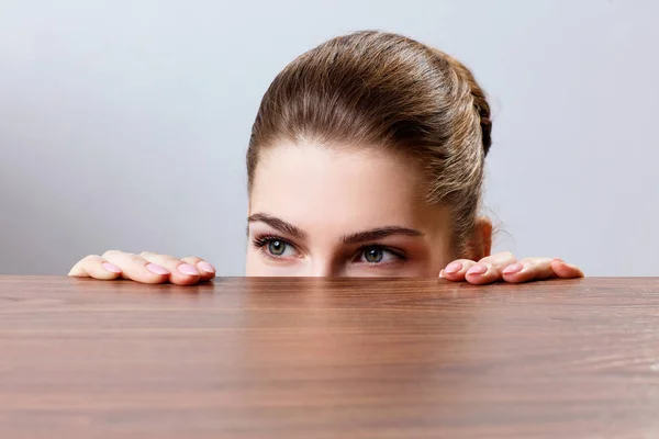 Mulher espreitando sob a borda da mesa de madeira — Fotografia de Stock