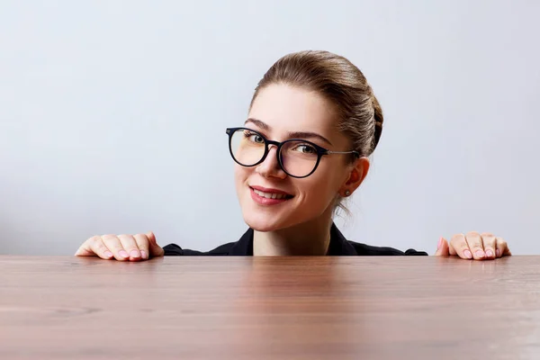 Kobieta w okularach ciekawski pod krawędzią drewniany stół. — Zdjęcie stockowe