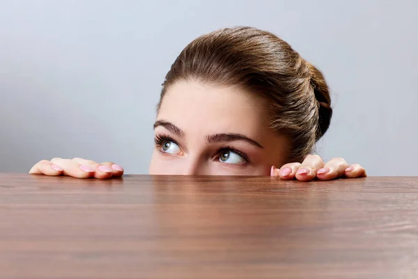Žena nakouknutí pod okraj dřevěného stolu — Stock fotografie
