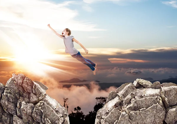 Little cute girl flying like a supergirl from one rock to another. — Stock Photo, Image