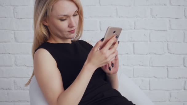 Jonge aantrekkelijke vrouw in zwarte jurk op zoek in smartphone. — Stockvideo