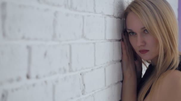 Yound schöne traurige Frau posiert in der Nähe der weißen Backsteinmauer. — Stockvideo
