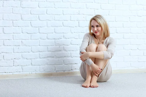 Härlig kvinna sitter på golvet över tegel vägg bakgrund. — Stockfoto