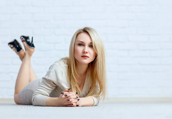 Sensual woman lying on floor against white brick wall. — Stock Photo, Image