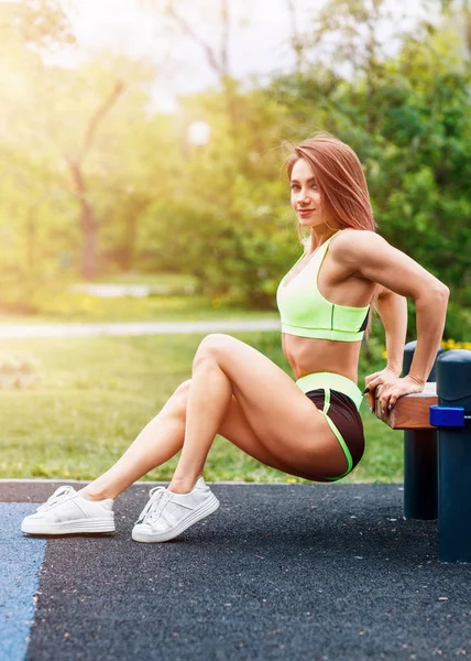 Jonge sportieve vrouw doen triceps duik oefening op stad straat bank. — Stockfoto