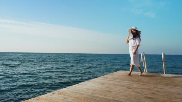 Jeune femme marchant sur une jetée en bois, regardant la mer . — Video