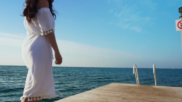 Jonge vrouw lopen op een houten pier, kijken naar de zee. — Stockvideo