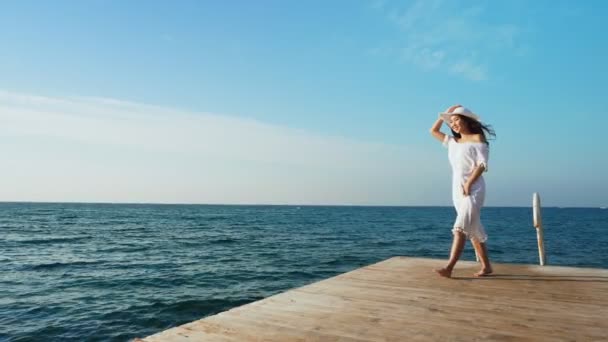 Jeune femme marchant sur une jetée en bois, regardant la mer . — Video