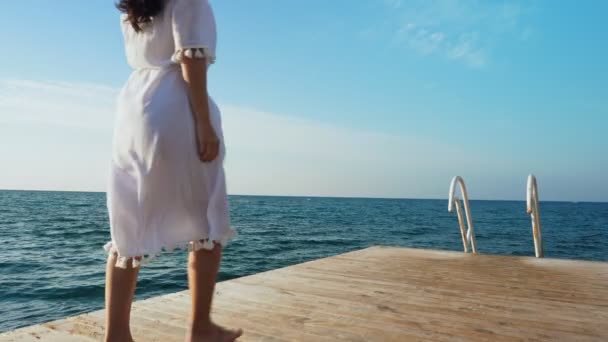 Mujer joven caminando sobre un muelle de madera, mirando al mar . — Vídeos de Stock