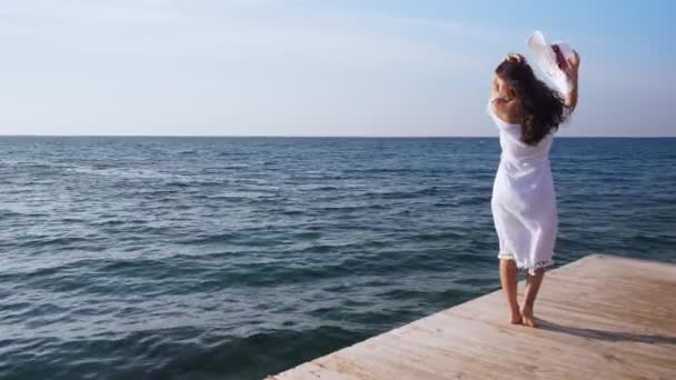 Jeune femme se tient sur une jetée en bois, regardant la mer . — Video