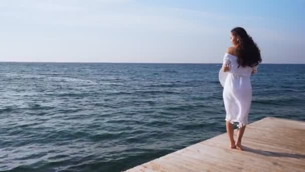 Mladá žena stojí na dřevěném molu, při pohledu na moře.