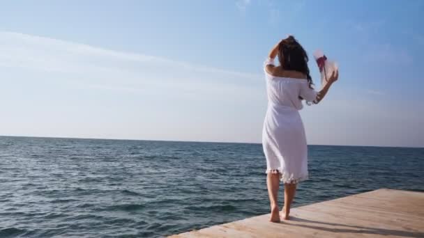Jonge vrouw in witte jurk staat op houten pier — Stockvideo