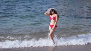 Plajda su kırmızı mayo giymiş kadın duruyor.