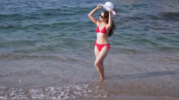 Femme vêtue de maillots de bain rouges se tient dans l'eau sur la plage . — Video