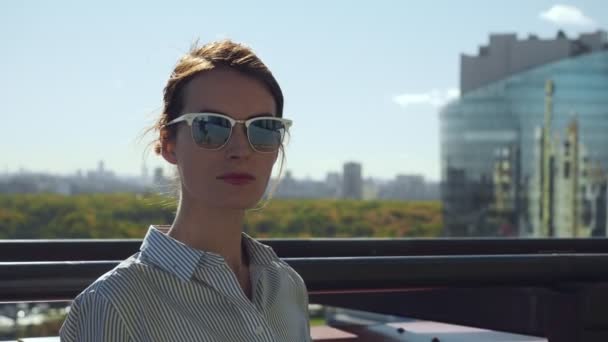 Junge Frau mit Sonnenbrille posiert auf Balkon eines Geschäftshauses. — Stockvideo