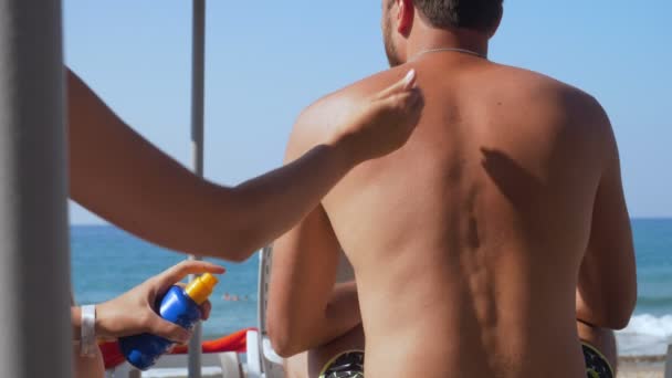 Namorada aplicando creme para seu namorado na praia . — Vídeo de Stock