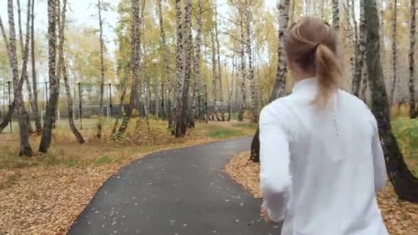 Mujer rubia joven corriendo en el parque de otoño . — Vídeos de Stock