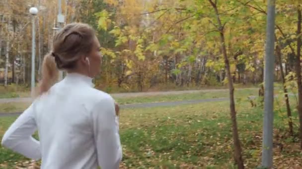 Young blonde woman running in the autumn park. — Stock Video